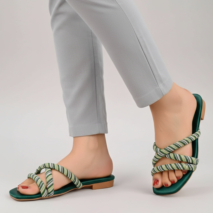 Green and white strappy sandals worn with light gray pants on a plain background