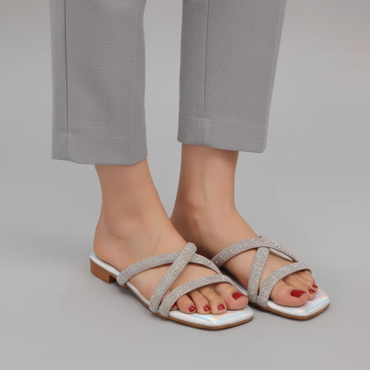 Silver strappy sandals worn with gray pants on a neutral background