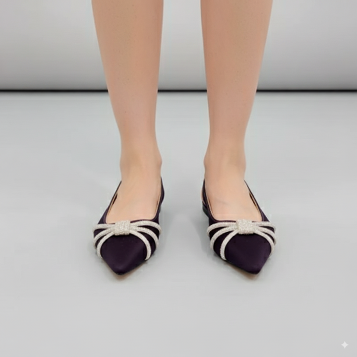 Purple pointed-toe flats with white bow details worn by a person on a light gray background