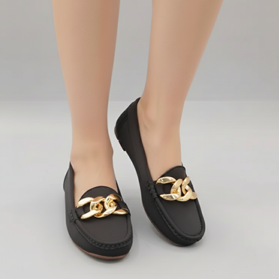 Black loafers with gold chain details worn by a person on a gray background