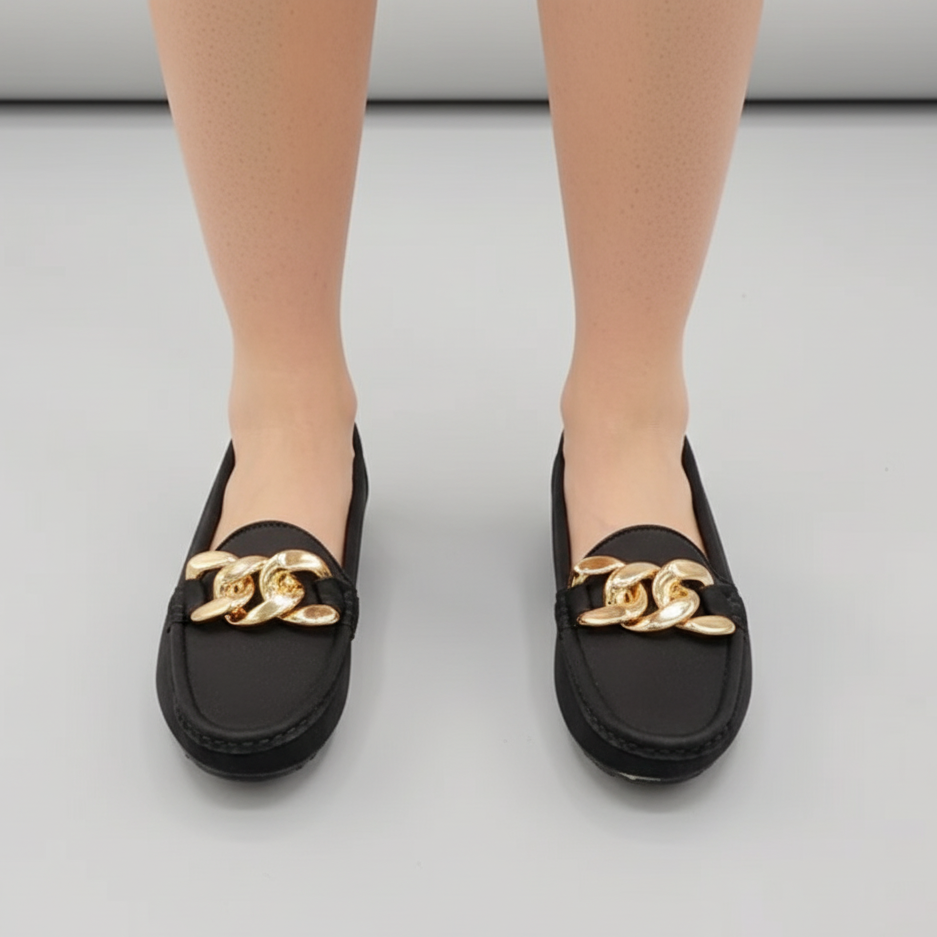 Black loafers with gold chain detail worn by a person on a light gray background