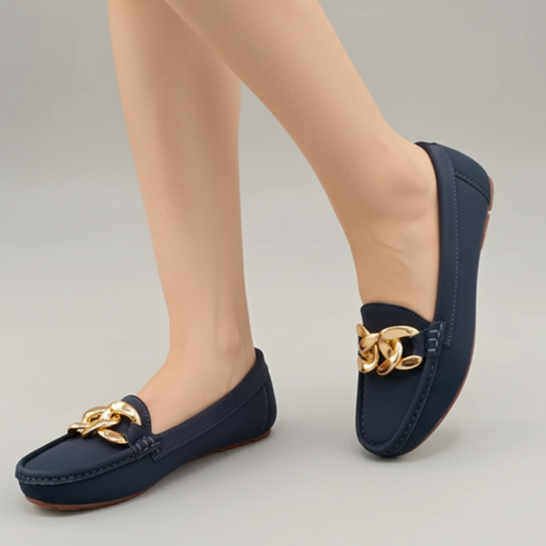 Navy loafers with gold chain detail worn by a person on a neutral background