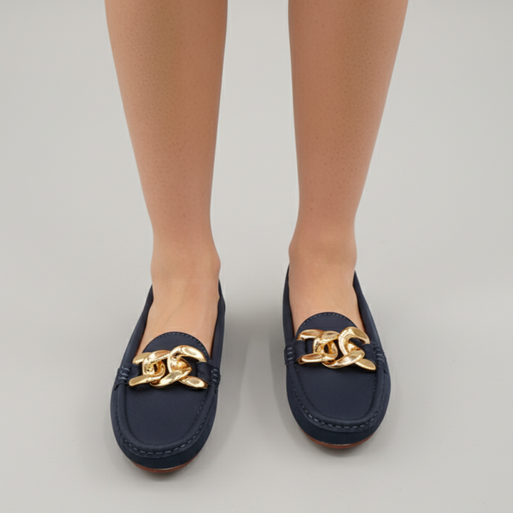 Navy loafers with gold chain detail worn by a person on a light gray background