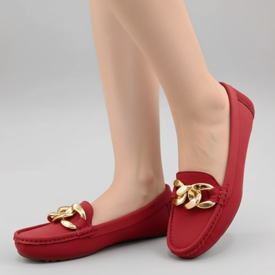 Red loafers with gold accents worn by a person on a gray background