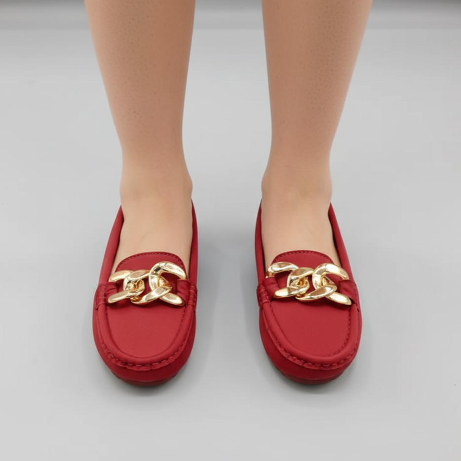 Red loafers with gold chain detail on a neutral background