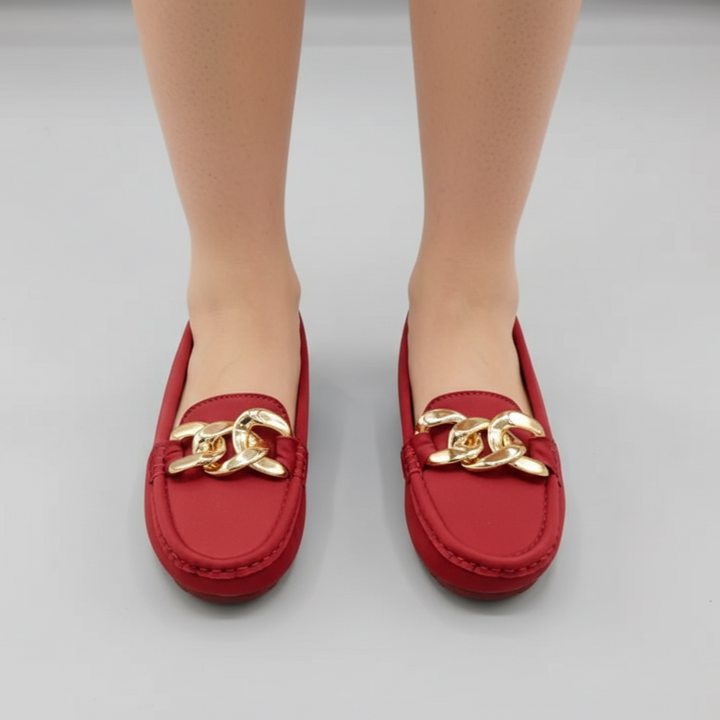 Red loafers with gold chain detail on a neutral background