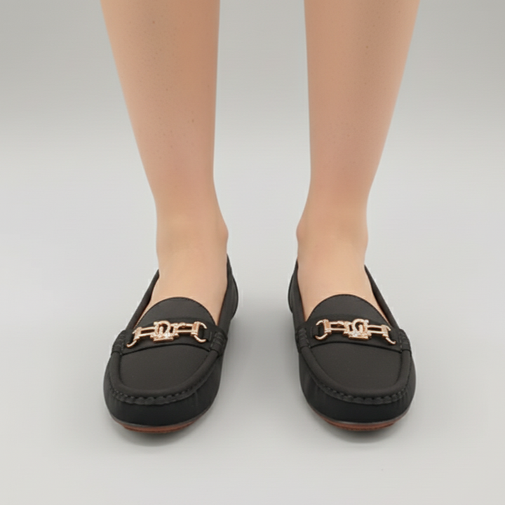 Black loafers with gold accents worn by a person on a light gray background