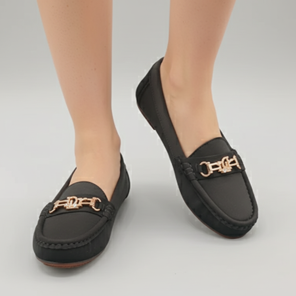 Black loafers with gold accents worn by a person on a gray background