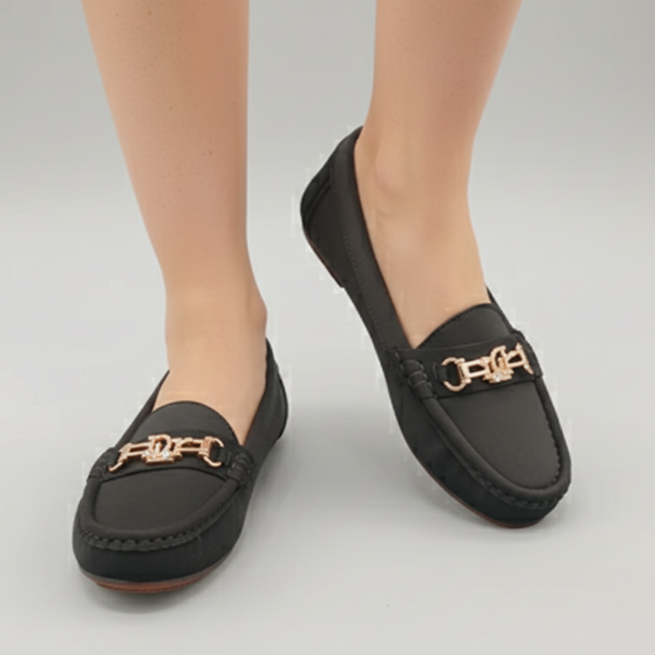 Black loafers with gold accents worn by a person on a gray background