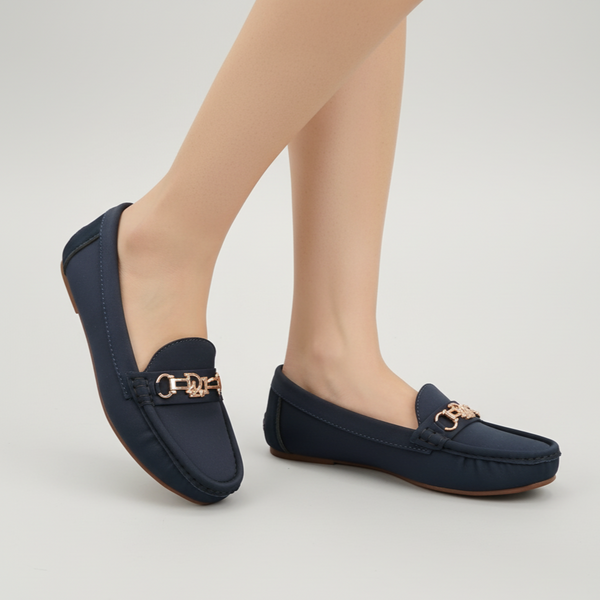 Navy loafers with gold buckles worn by a person on a light gray background