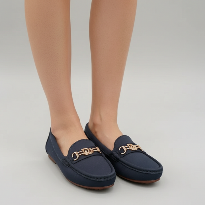 Navy loafers with gold accents worn by a person on a light gray background