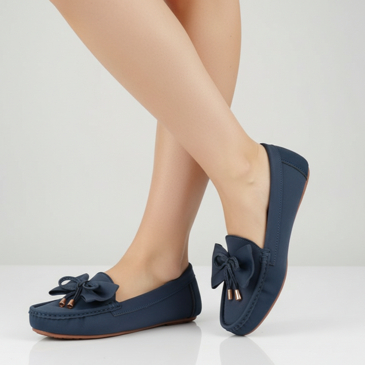 Navy blue loafers with bow details worn by a person on a light gray background