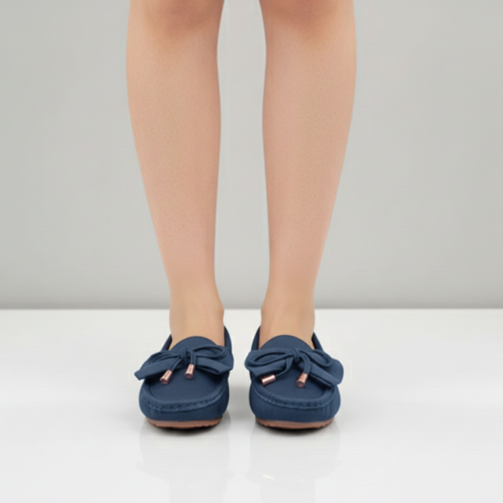 Blue loafers with bow details worn by a person on a white background