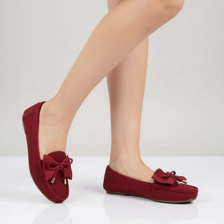 Red loafers with bow details worn by a person on a light gray background