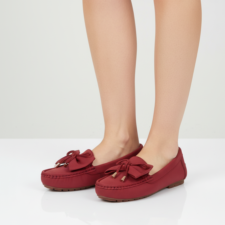Red loafers with bow details worn by a person on a white background