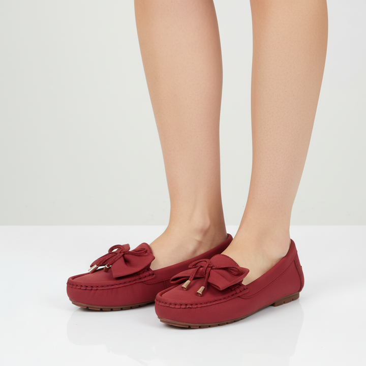 Red loafers with bow details worn by a person on a white background