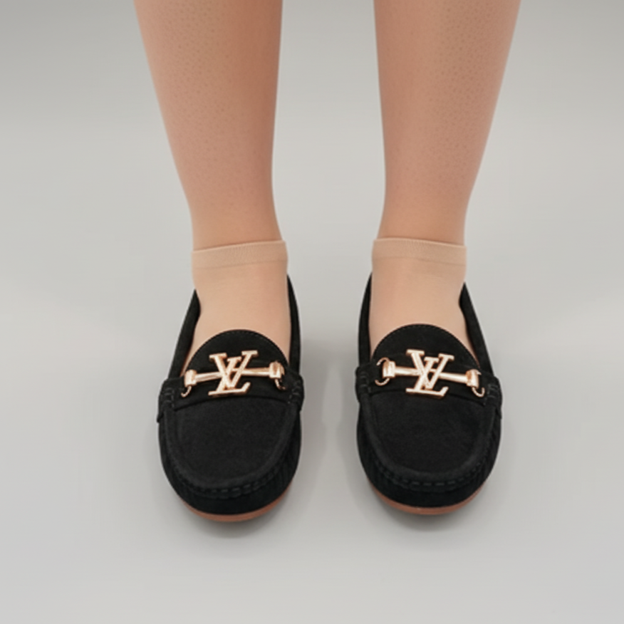 Black loafers with gold accents worn by a person on a light gray background