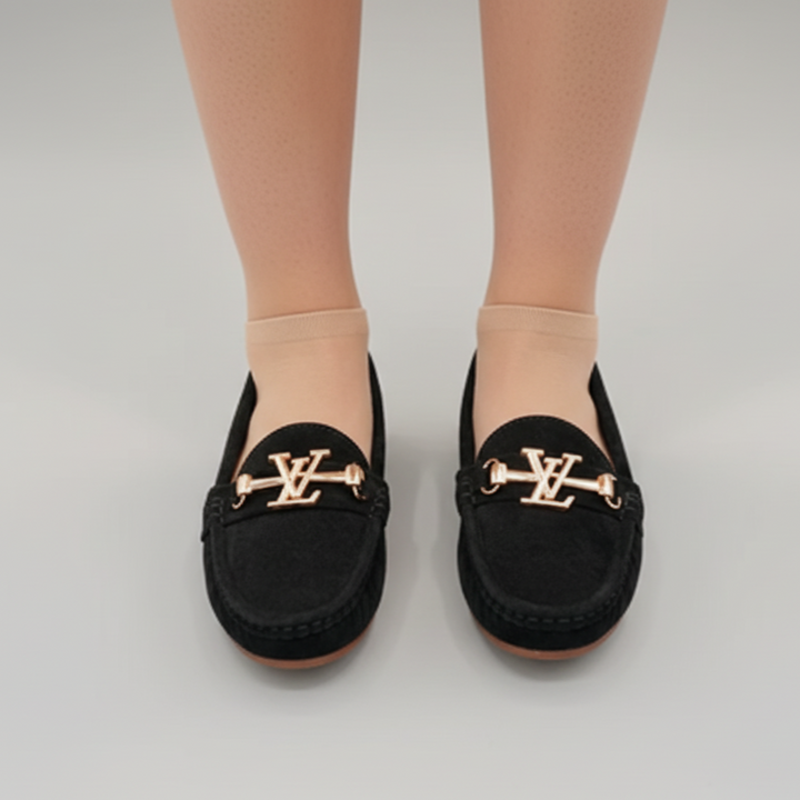 Black loafers with gold accents worn by a person on a light gray background