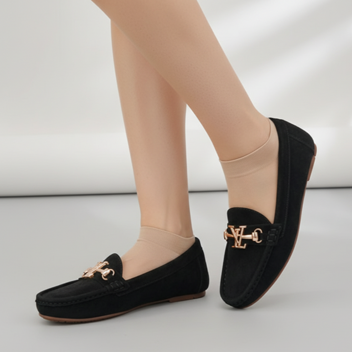 Black loafers with gold accents worn by a person on a light gray background