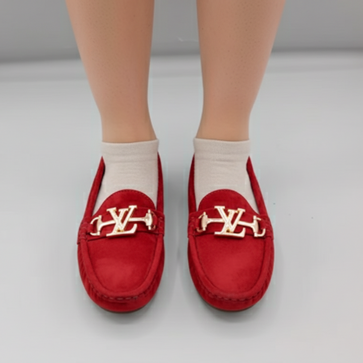 Red loafers with gold accents worn by a person on a light gray background