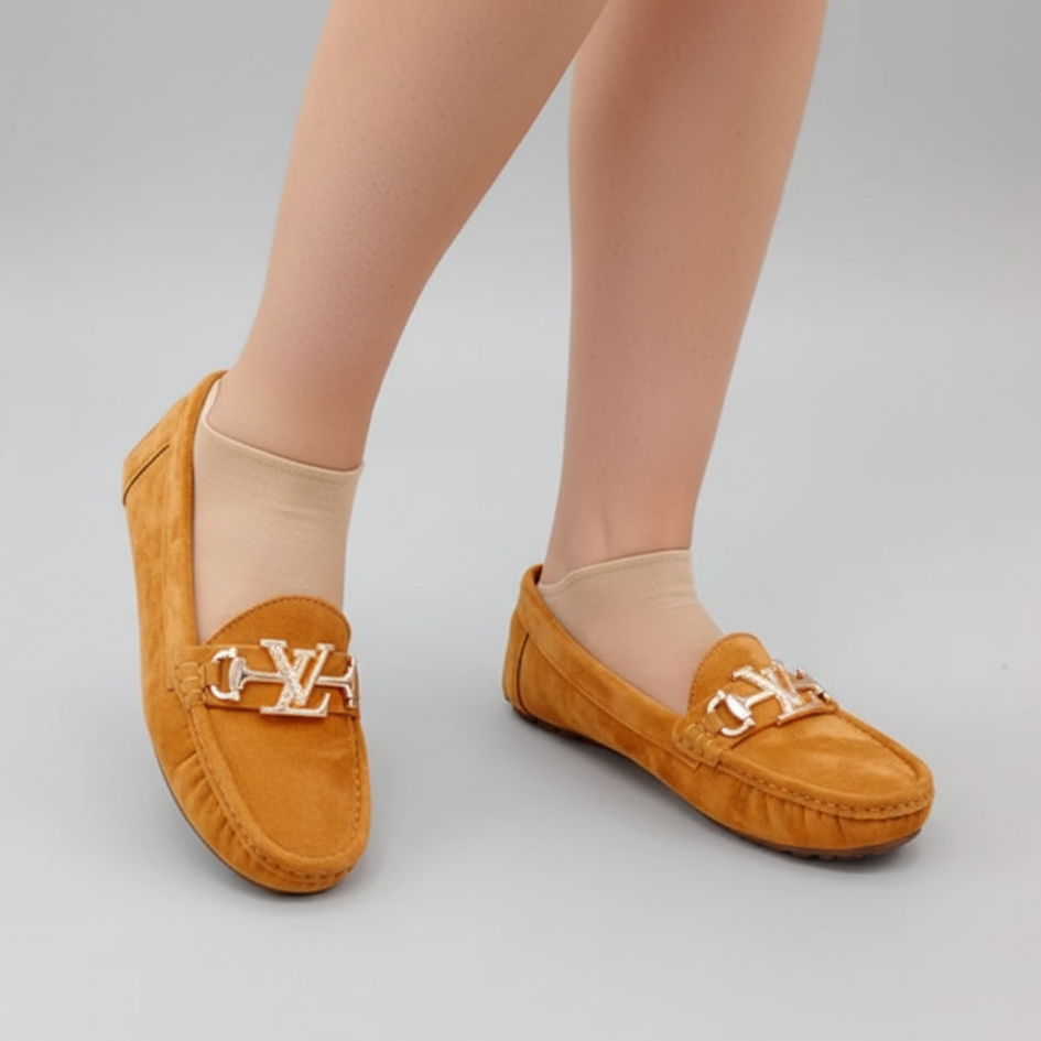 Brown loafers with a gold chain detail worn by a person on a gray background