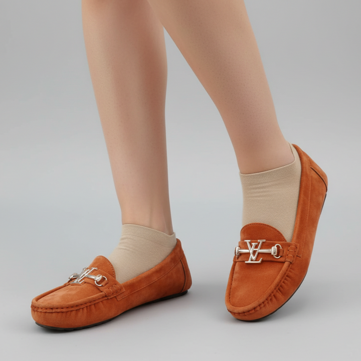 Orange loafers with a decorative buckle worn by a person on a gray background