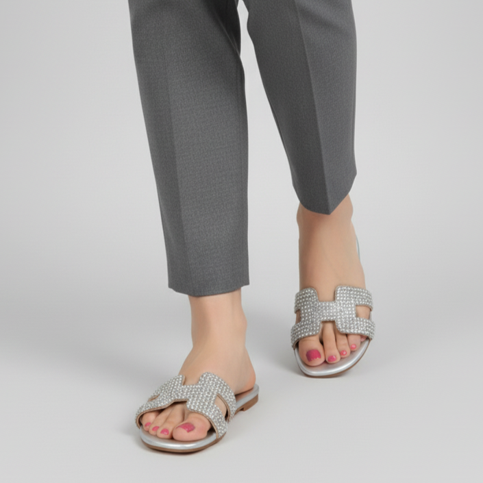 Person wearing gray pants and silver sandals on a plain background