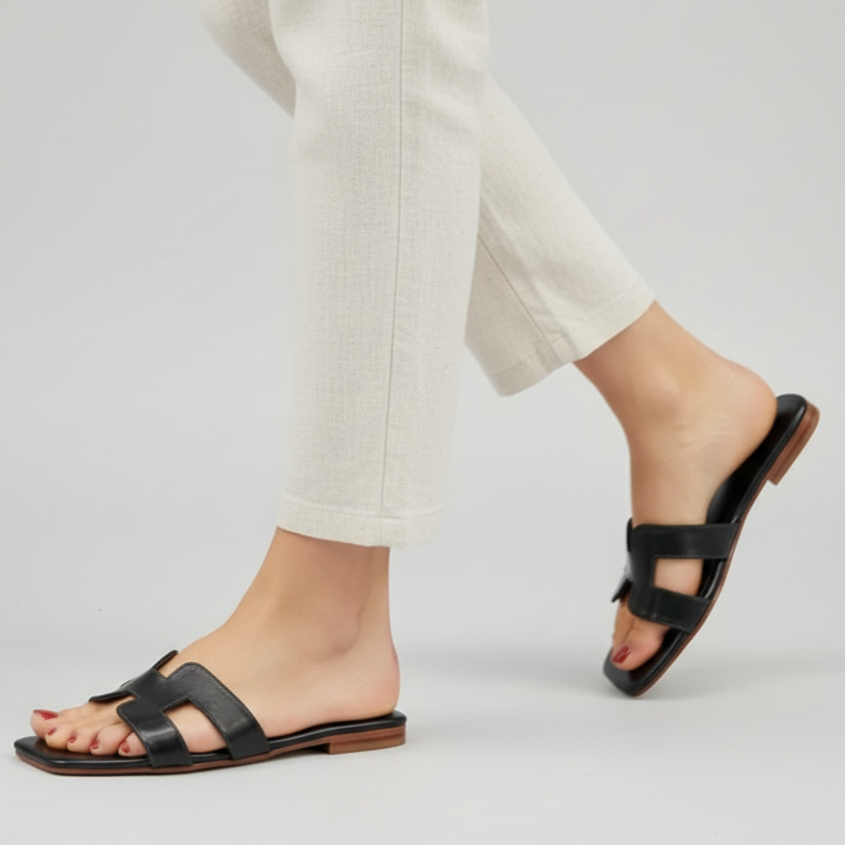 Black sandals worn with light-colored pants on a plain background