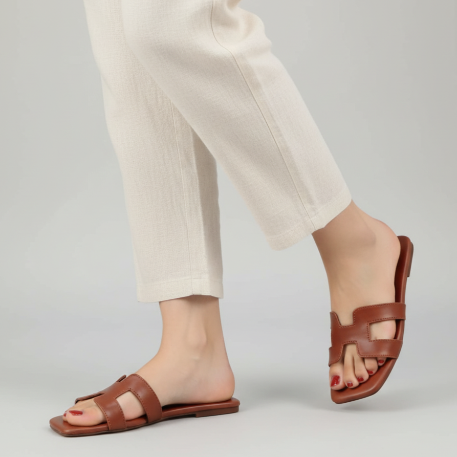 Brown sandals worn with white pants on a light gray background