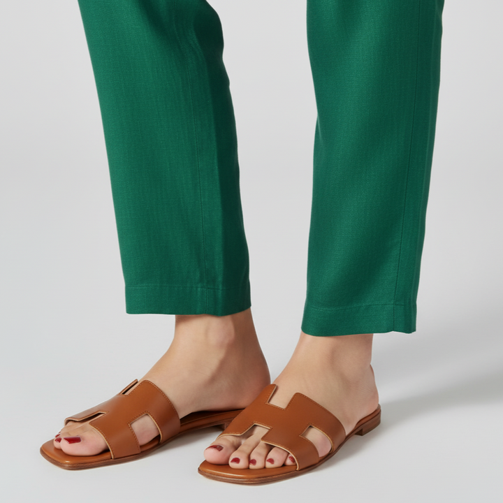Brown sandals worn with green pants on a light gray background