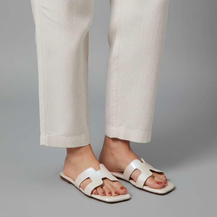 White sandals worn with light-colored pants on a gray background