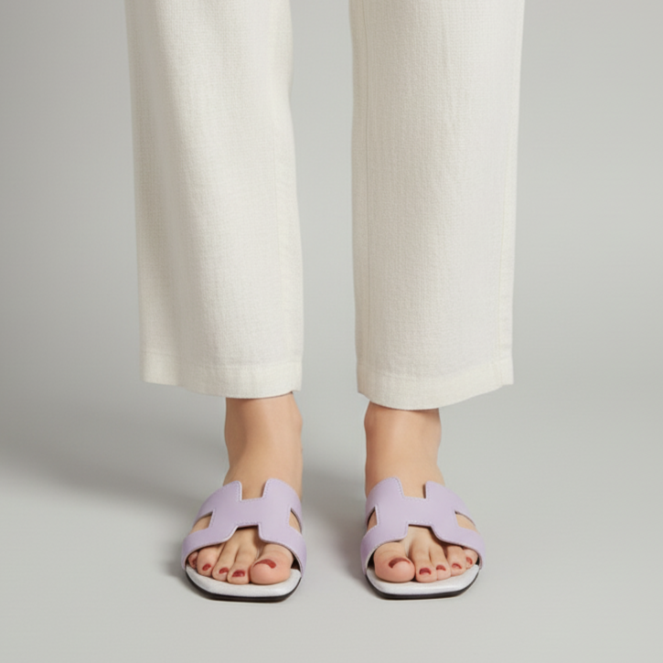 Person wearing light purple sandals and white pants on a plain background