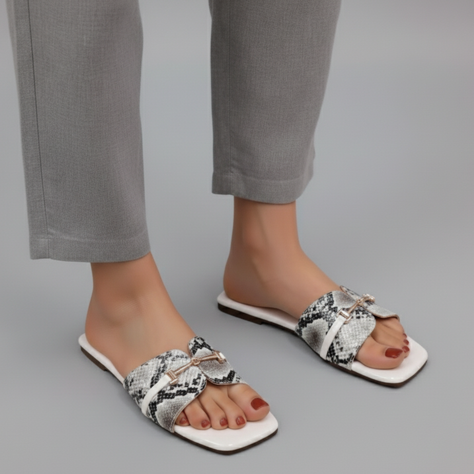 White sandals with snake print worn by a person on a gray background