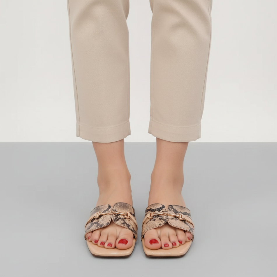 Person wearing snake print sandals with beige pants on a plain background
