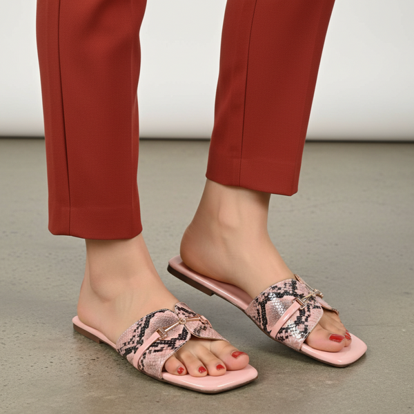 Pink sandals with snake print worn by a person in red pants on a neutral background