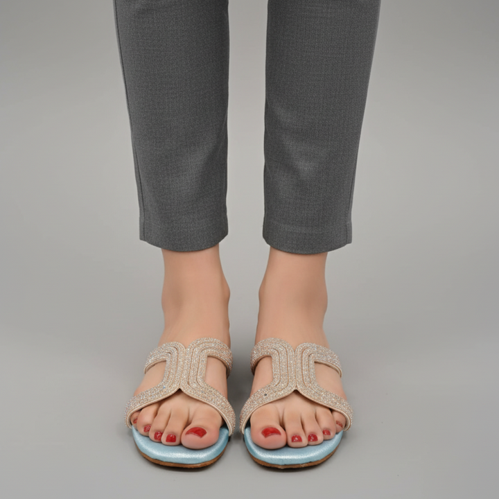 Beige sandals with blue soles worn with gray pants on a neutral background