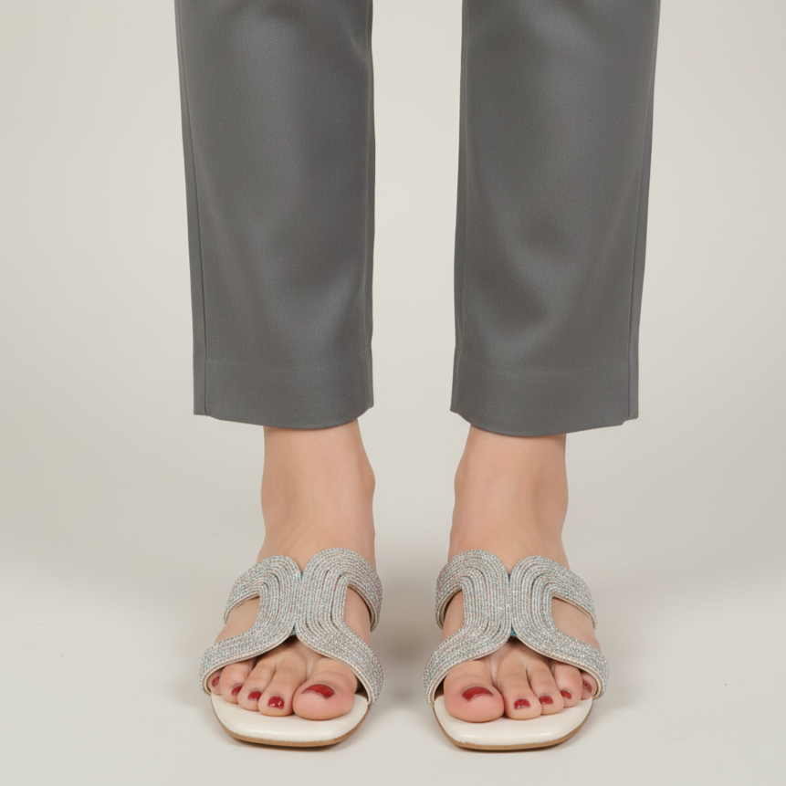 Silver sandals worn with gray pants on a plain background