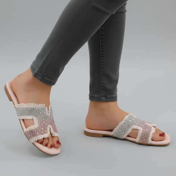 Pink sandals with rhinestone details worn with gray pants on a gray background