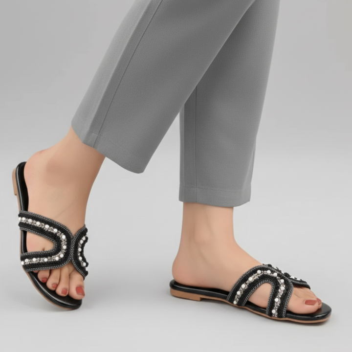 Black sandals with embellishments worn with gray pants on a light gray background