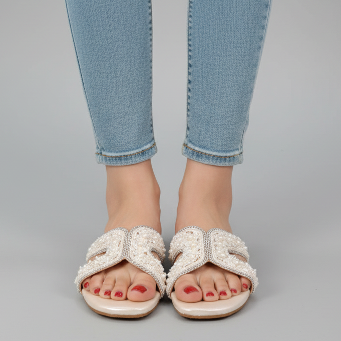 Person wearing light blue jeans and white sandals on a gray background