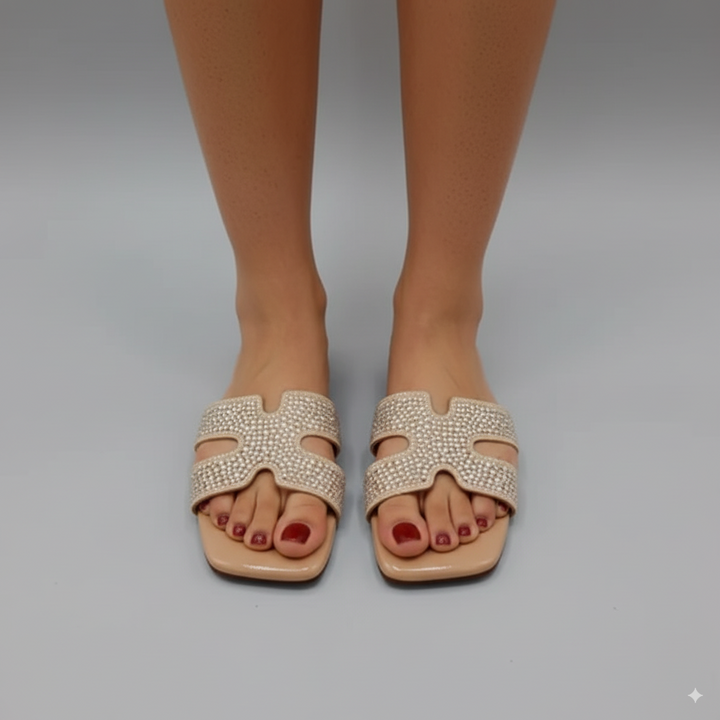 Beige sandals with rhinestone embellishments worn by a person on a gray background