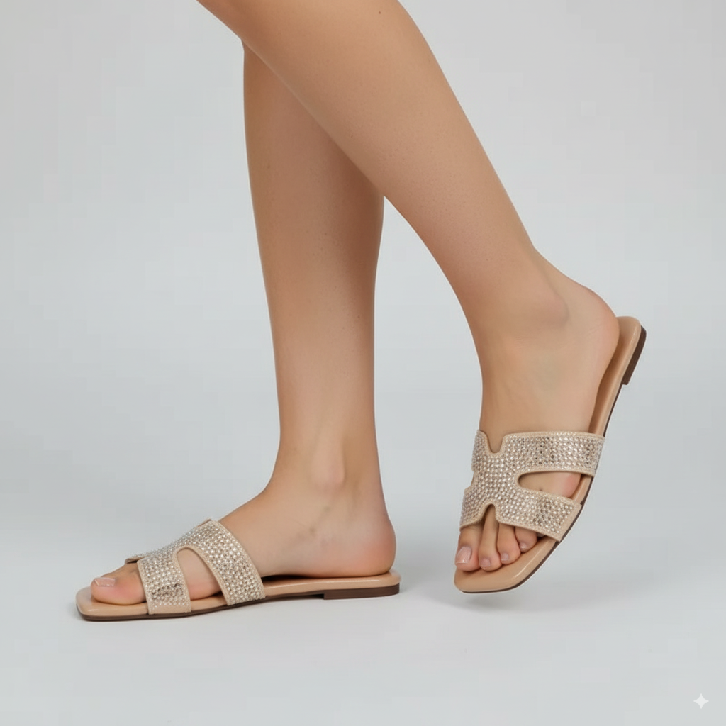 Beige sandals with rhinestone details worn by a person on a light gray background