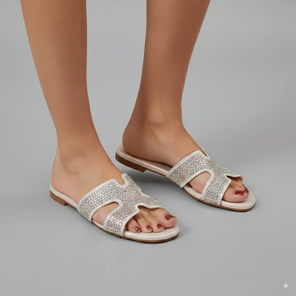Silver embellished sandals worn by a person on a gray background