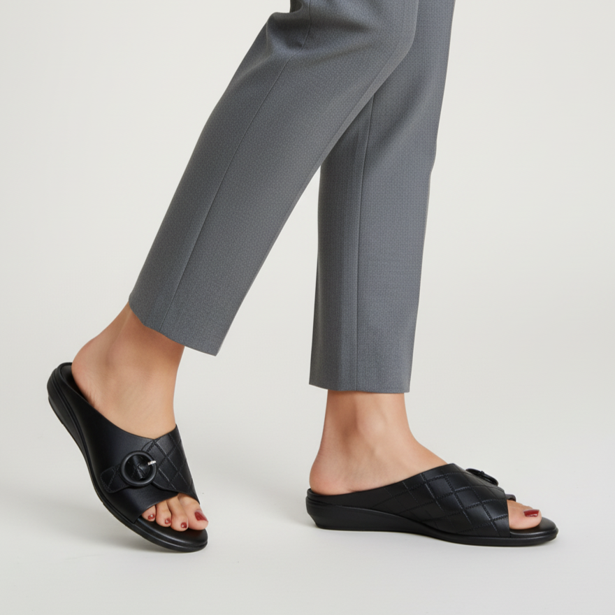 Person wearing black sandals and gray pants on a light gray background