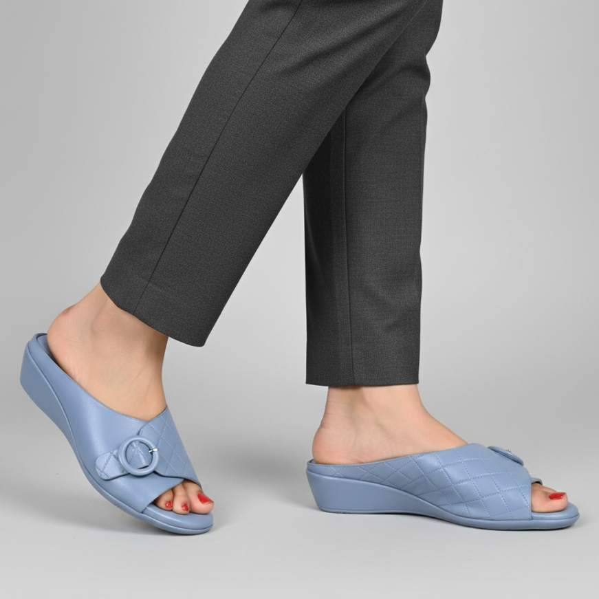 Person wearing light blue slides with dark gray pants on a plain background