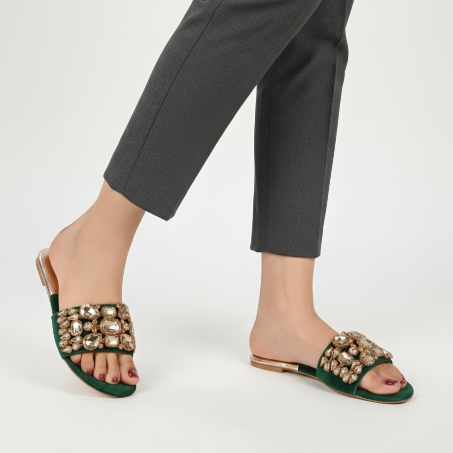 Green sandals with embellishments worn with gray pants on a white background