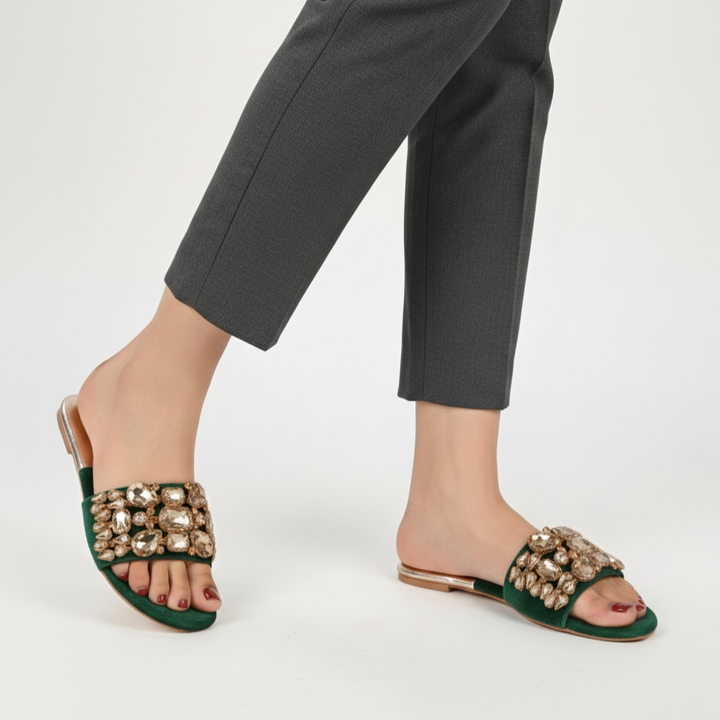 Green sandals with embellishments worn with gray pants on a white background