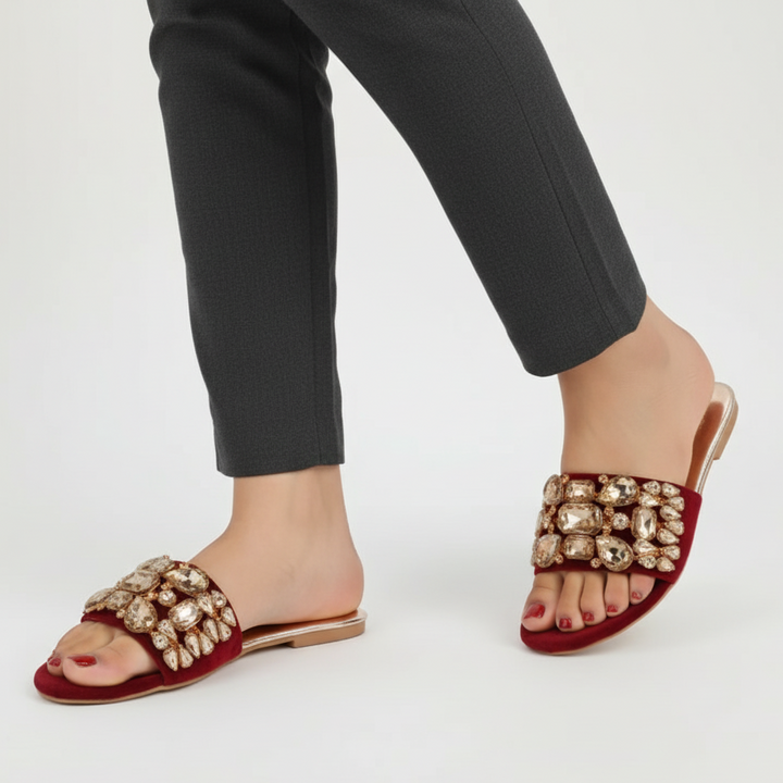Red embellished sandals worn with black pants on a white background