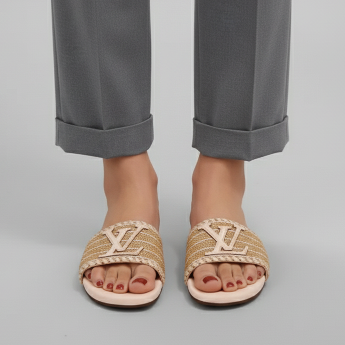 Person wearing beige sandals with a brand logo, paired with gray pants on a light gray background