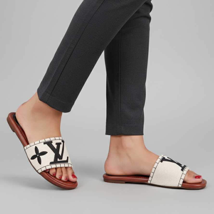 White sandals with black pattern worn by a person in dark pants on a gray background